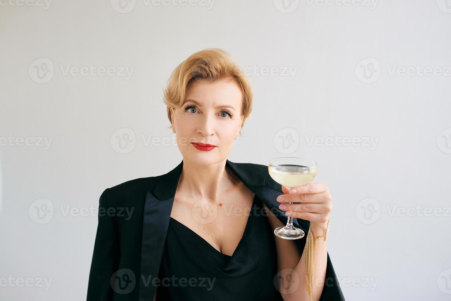 mujer madura elegante con estilo en esmoquin con una copa de vino espumoso. fiesta, celebración, concepto anti edad. foto