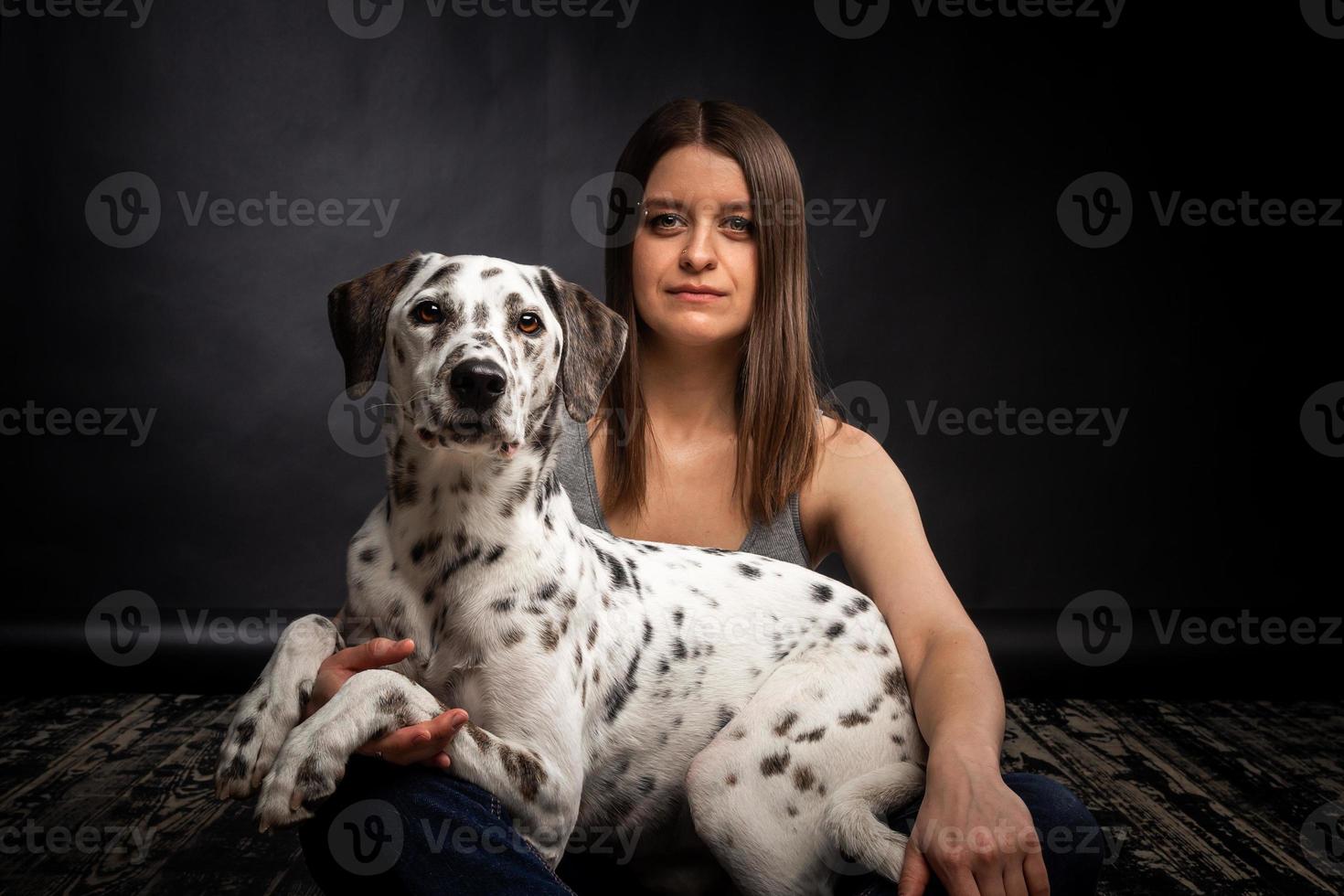 A young pretty woman is playing with her Dalmatian pet, isolated on a black background. photo