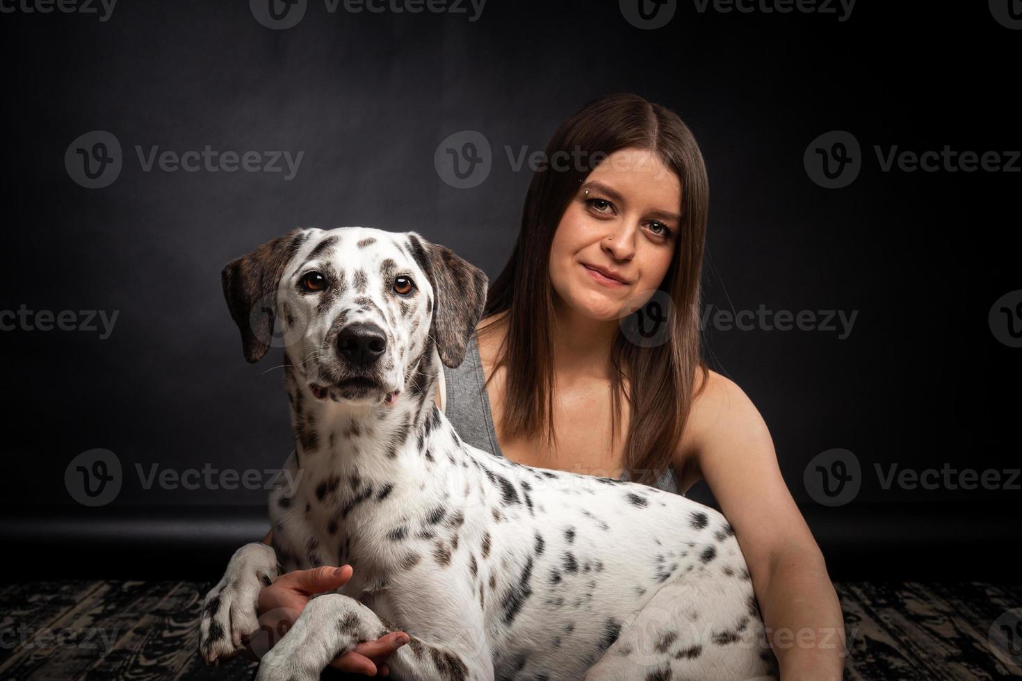 una joven mujer bonita está jugando con su mascota dálmata, aislada en un fondo negro. foto