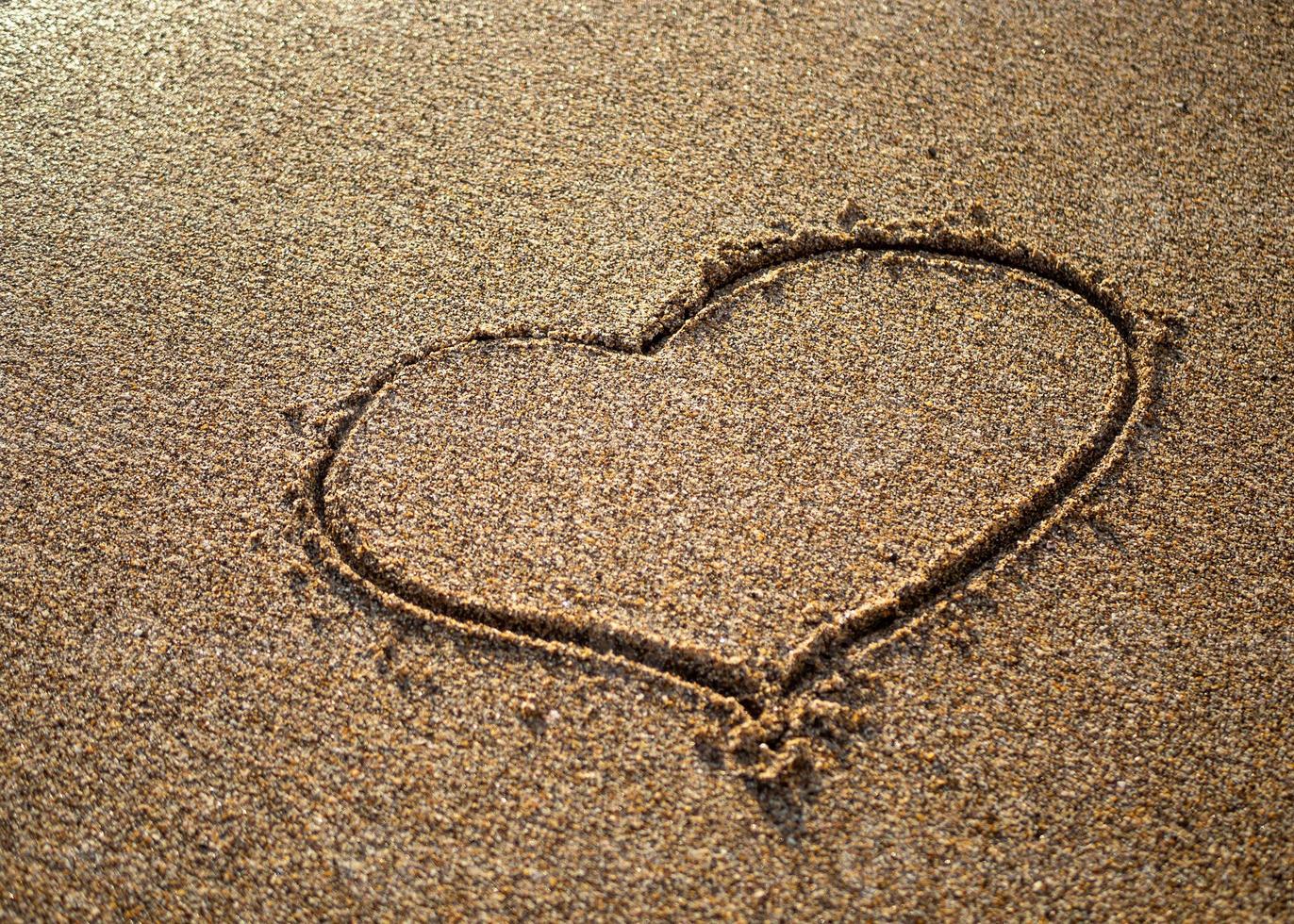 Heart on a sand of beach with wave on background photo
