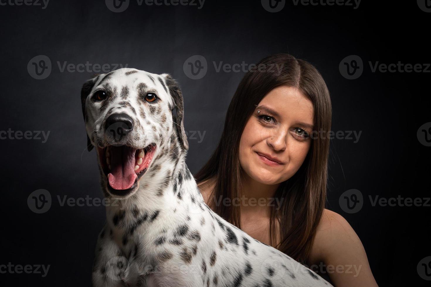 una joven mujer bonita está jugando con su mascota dálmata, aislada en un fondo negro. foto