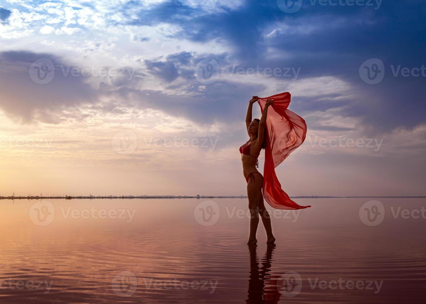 Silhouette of a girl in a red swimsuit on the beach. Red tissue develops in her hands. photo