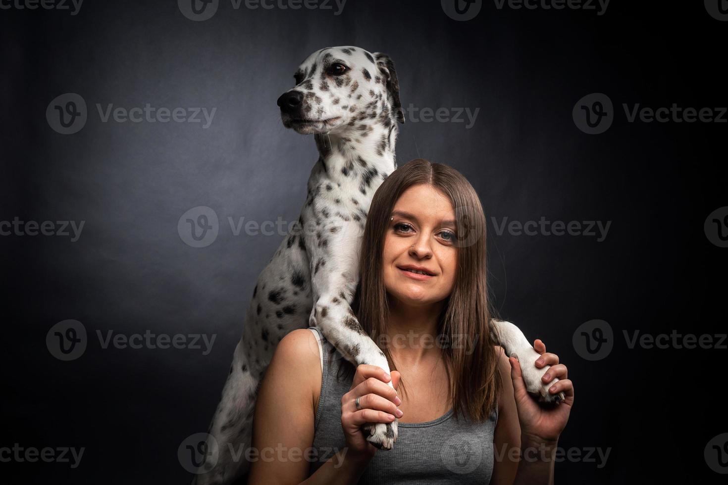 A young pretty woman is playing with her Dalmatian pet, isolated on a black background. photo