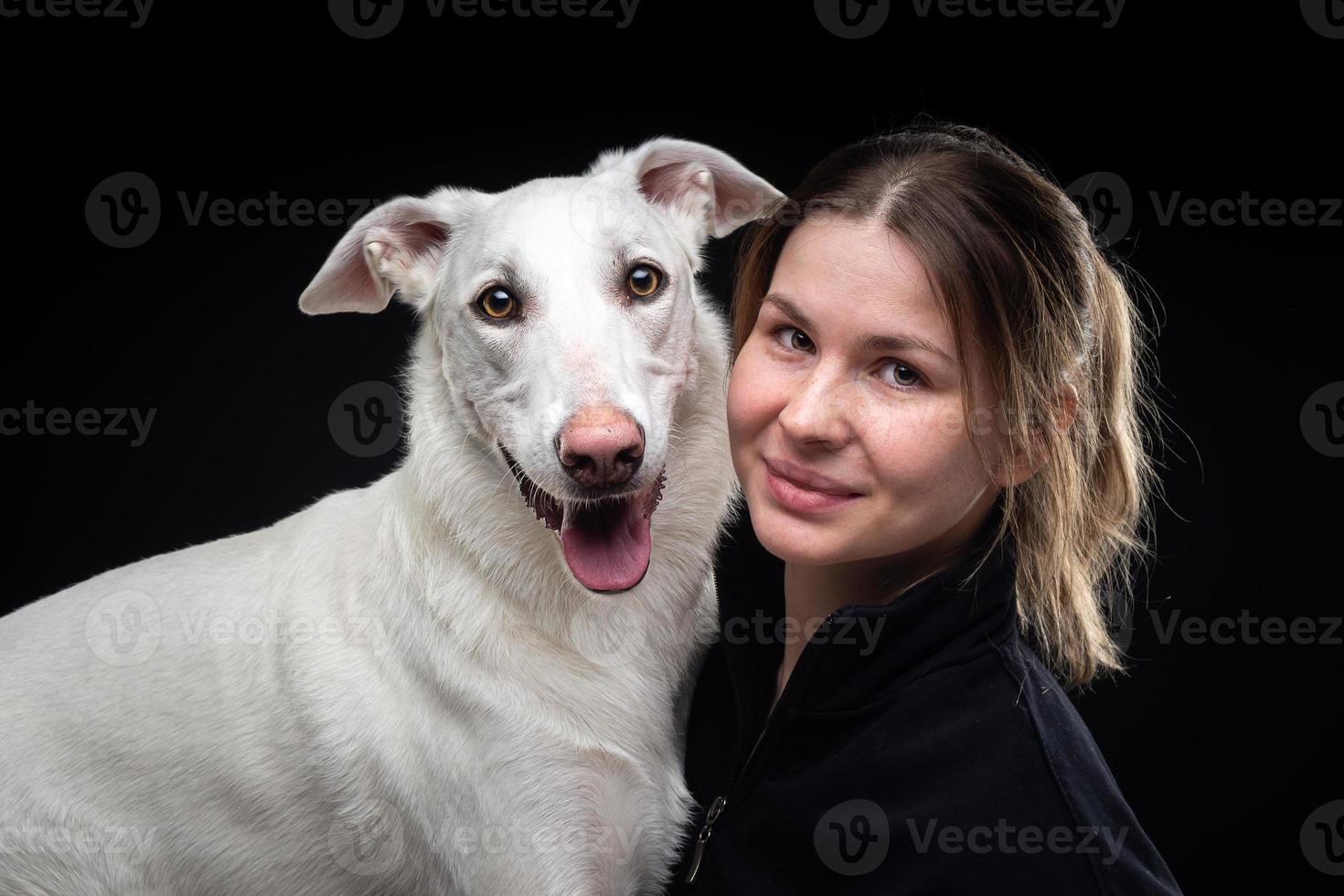 joven mujer bonita posa con su mascota blanca, resaltada en un fondo negro. foto