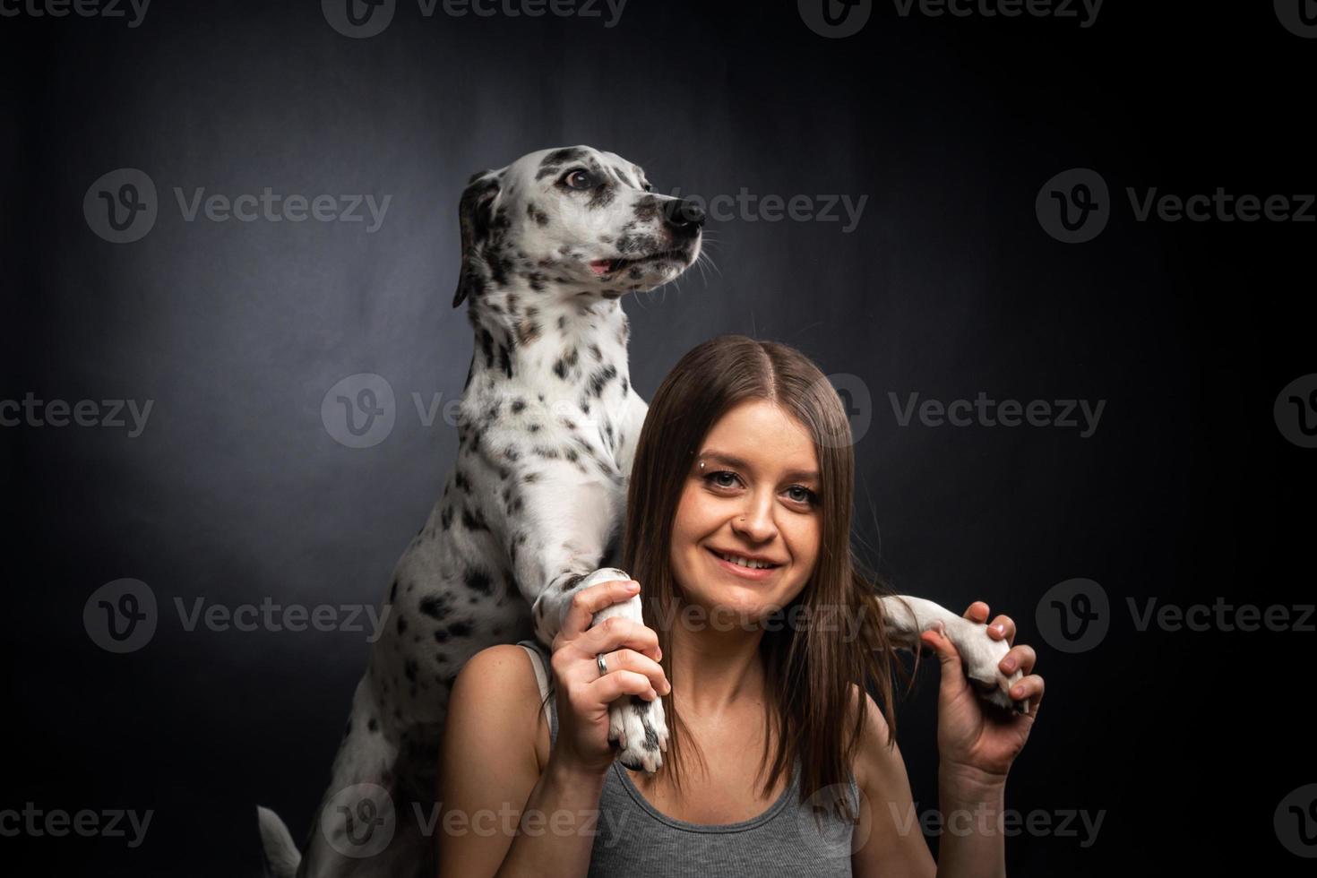 A young pretty woman is playing with her Dalmatian pet, isolated on a black background. photo