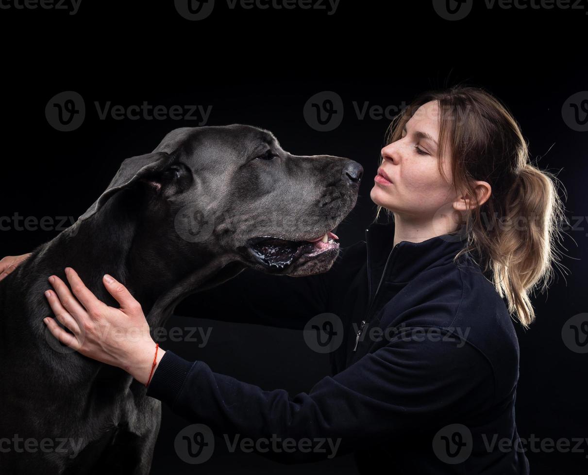 young pretty woman poses with her pet, a Great Dane, highlighted on a black background. photo