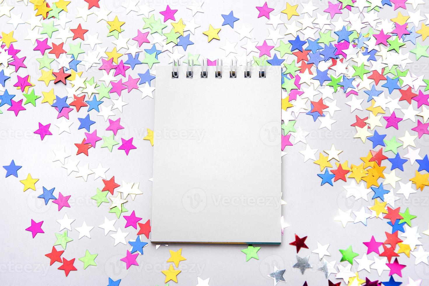 White notebook on a white background with scattered multicolored glitter stars. Place for text photo