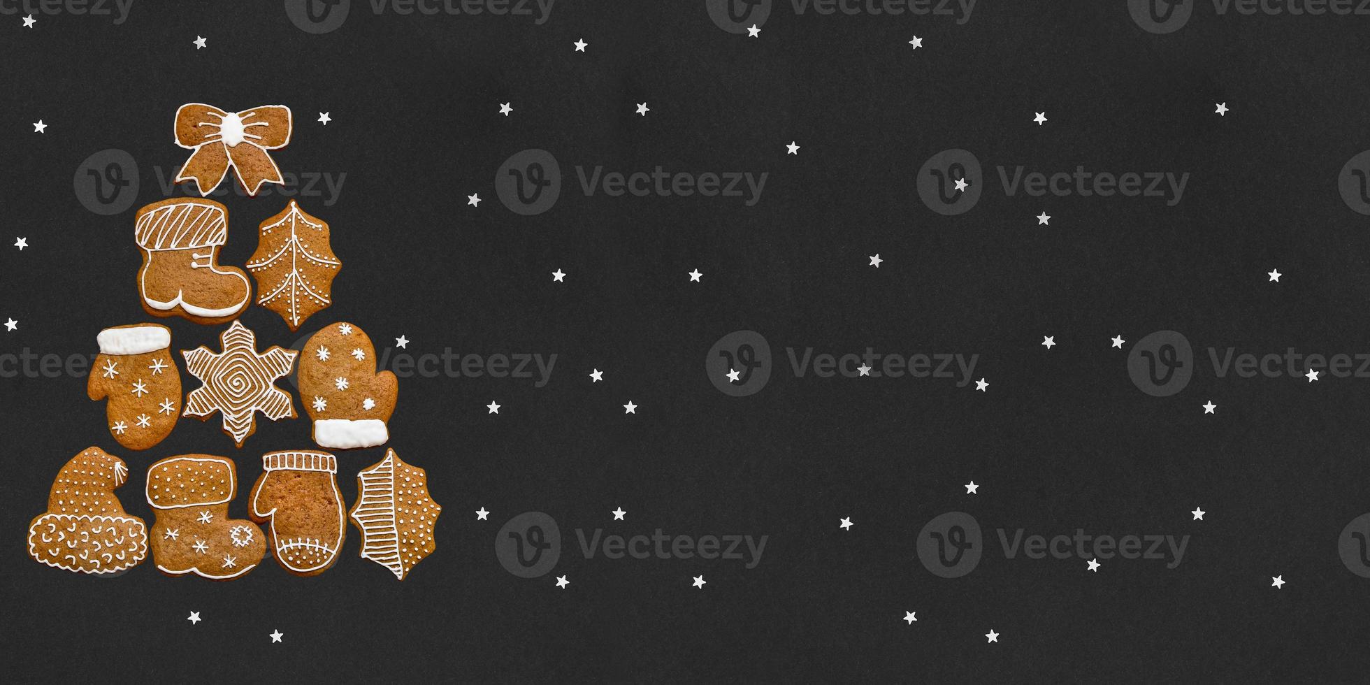 Christmas tree made up of gingerbread cookies on a black background with stars. Place for your text photo