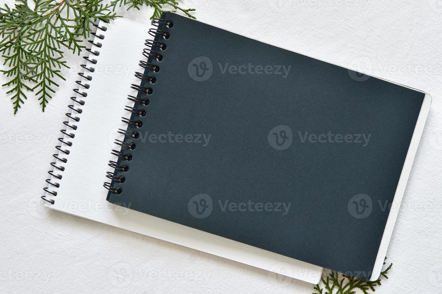 black and white sketchbook on a spring lying on a linen tablecloth with sprigs of green thuja photo