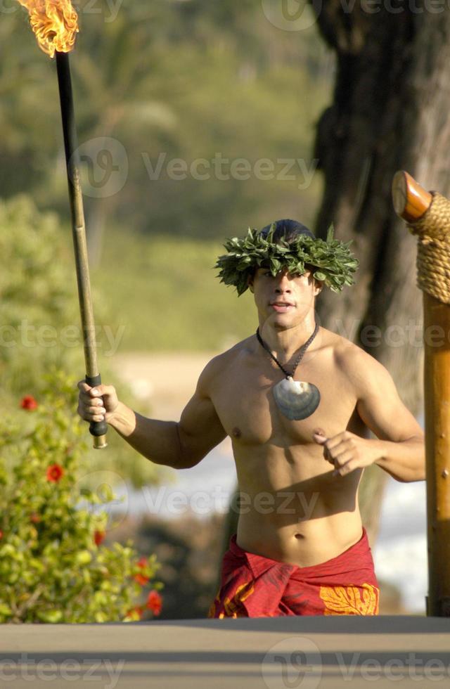 A male hula dancer runs with a tiki torch to light the stages lights for the performance. photo