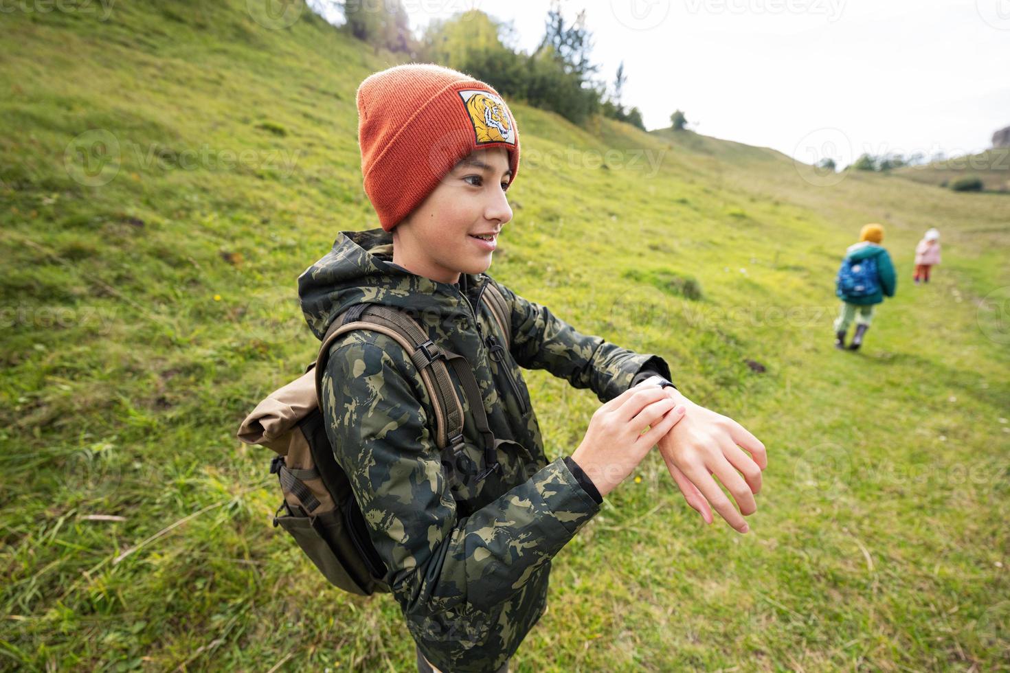 Boy with bacpack looking at his smart watches while hiking. photo