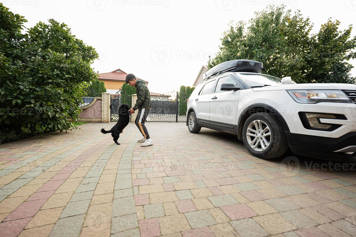 Boy playing with his dog in the yard of house, near family car. photo