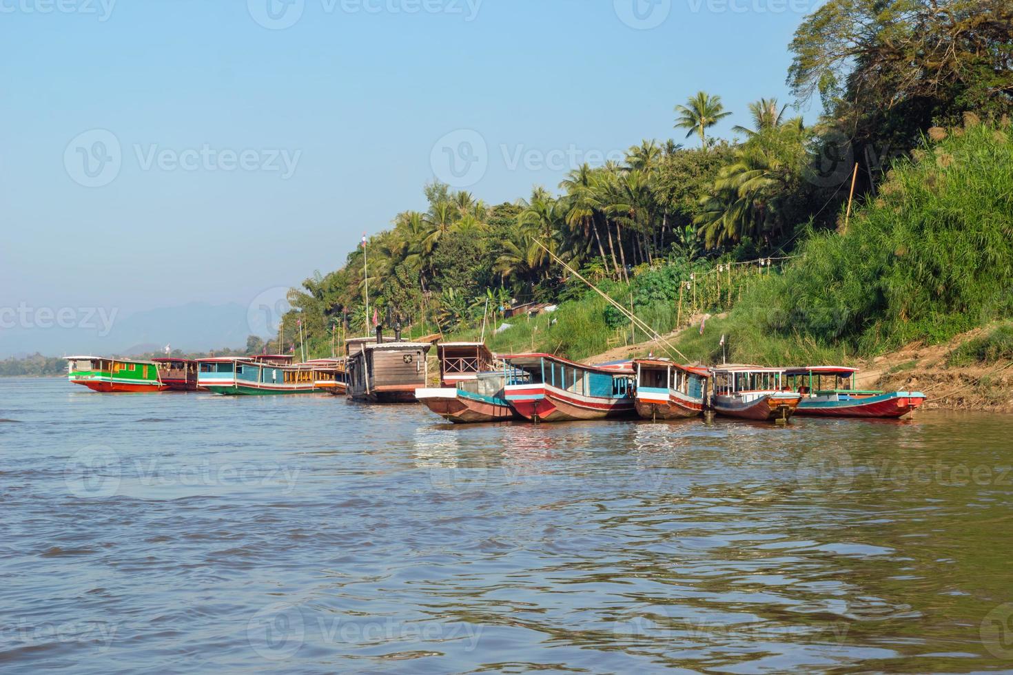 paisaje tropical con botes de cola larga en el río, palmeras en la orilla y montañas en el horizonte. río mekong, luang prabang, laos. foto