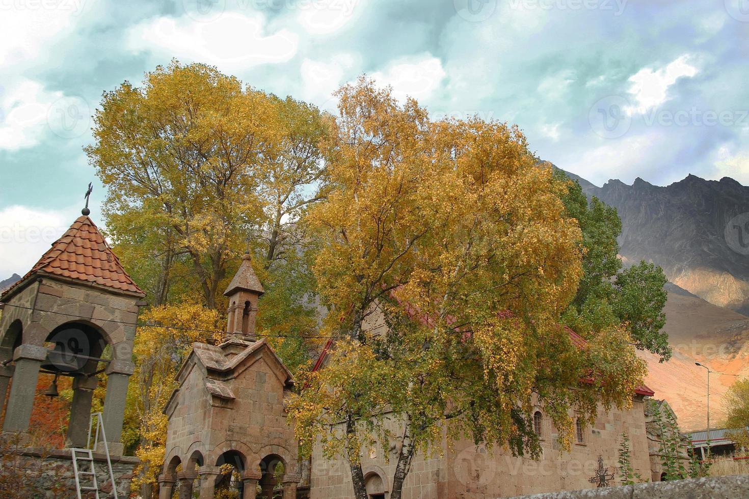 View on Medieval Orthodox Church with autumn trees on a background of mountains in cloudy weather. Caucasus Mountains, Georgia. photo