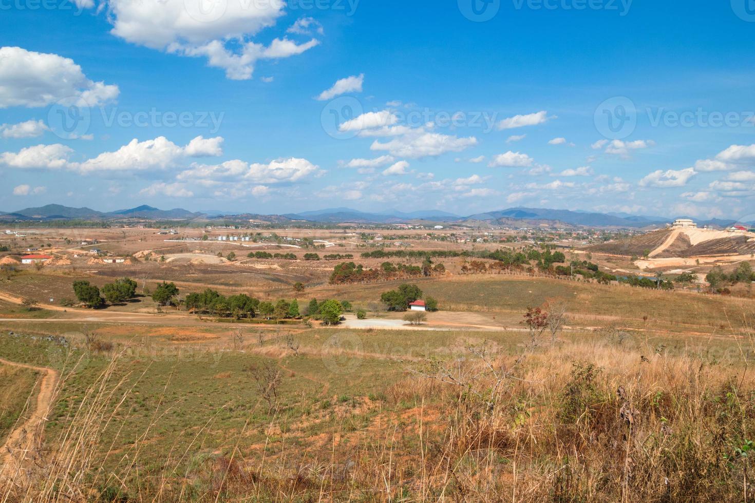 paisaje rural con montañas, campos, pueblo sobre fondo de cielo azul nublado. phonsovan, laos. foto