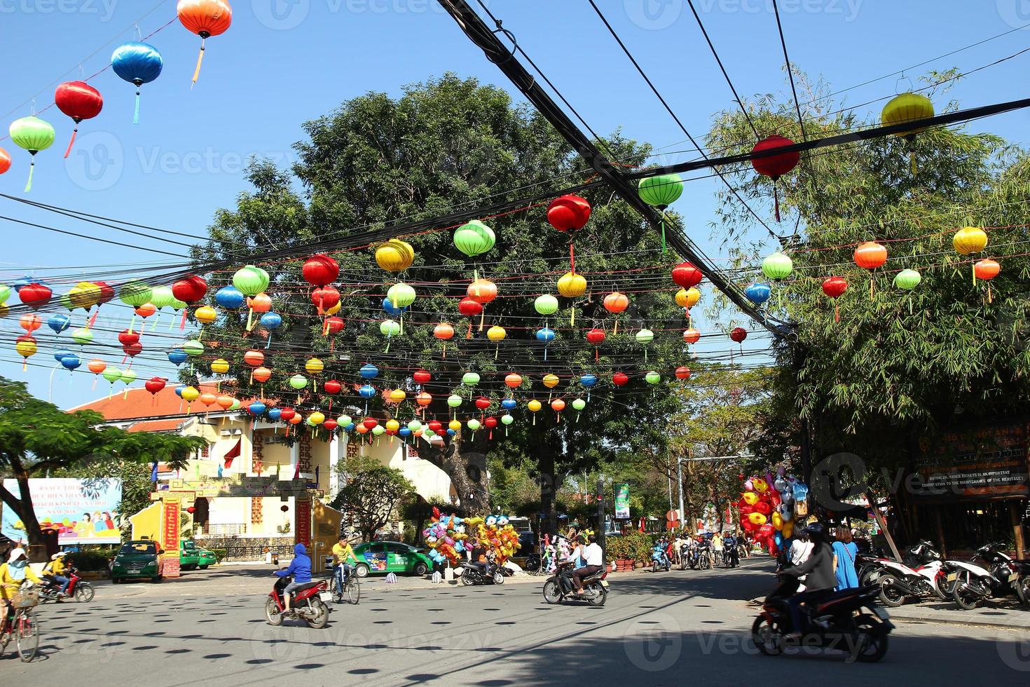 Hoi An, Vietnam - February 15, 2018. View on a busy crossroad in a center of city with motorcyclists, bicyclists, Festive colorful decorations for celebrating Tet - Vietnamese New Year. photo