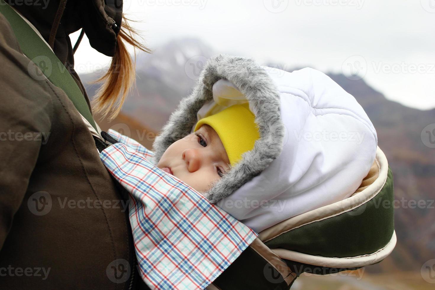 Portrait of little girl in ergo carrier with her mother on a background of autumn mountains. photo