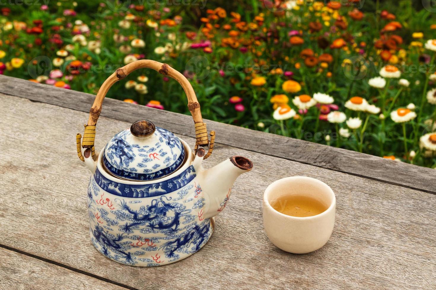 tetera china y taza con té verde sobre una mesa de madera sobre un fondo de flores de colores brillantes, vista superior. Pai, Tailandia. foto