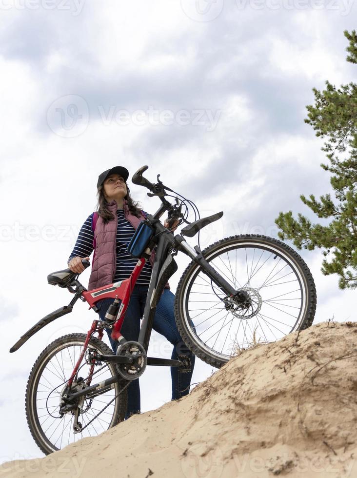 A young, pretty woman on a bicycle was climbing a sand dune, looking somewhere photo