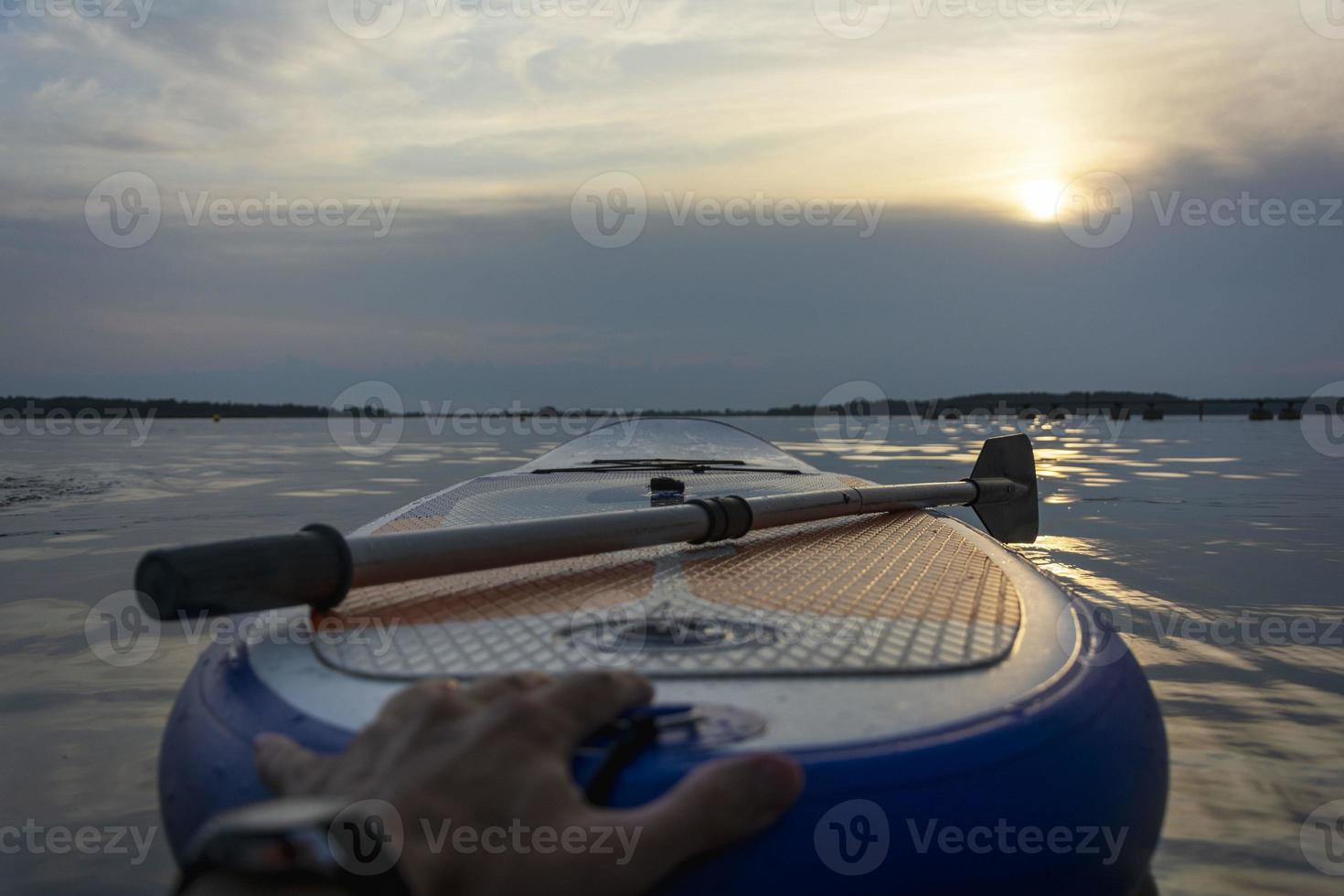 SUP board, Paddle board with a paddle in the sunset light on the background of water close-up. SUP boarding equipment. photo