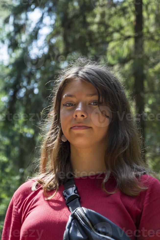 Portrait of a cute European teenage girl in the forest in summer on a sunny day, a girl in a burgundy dress photo