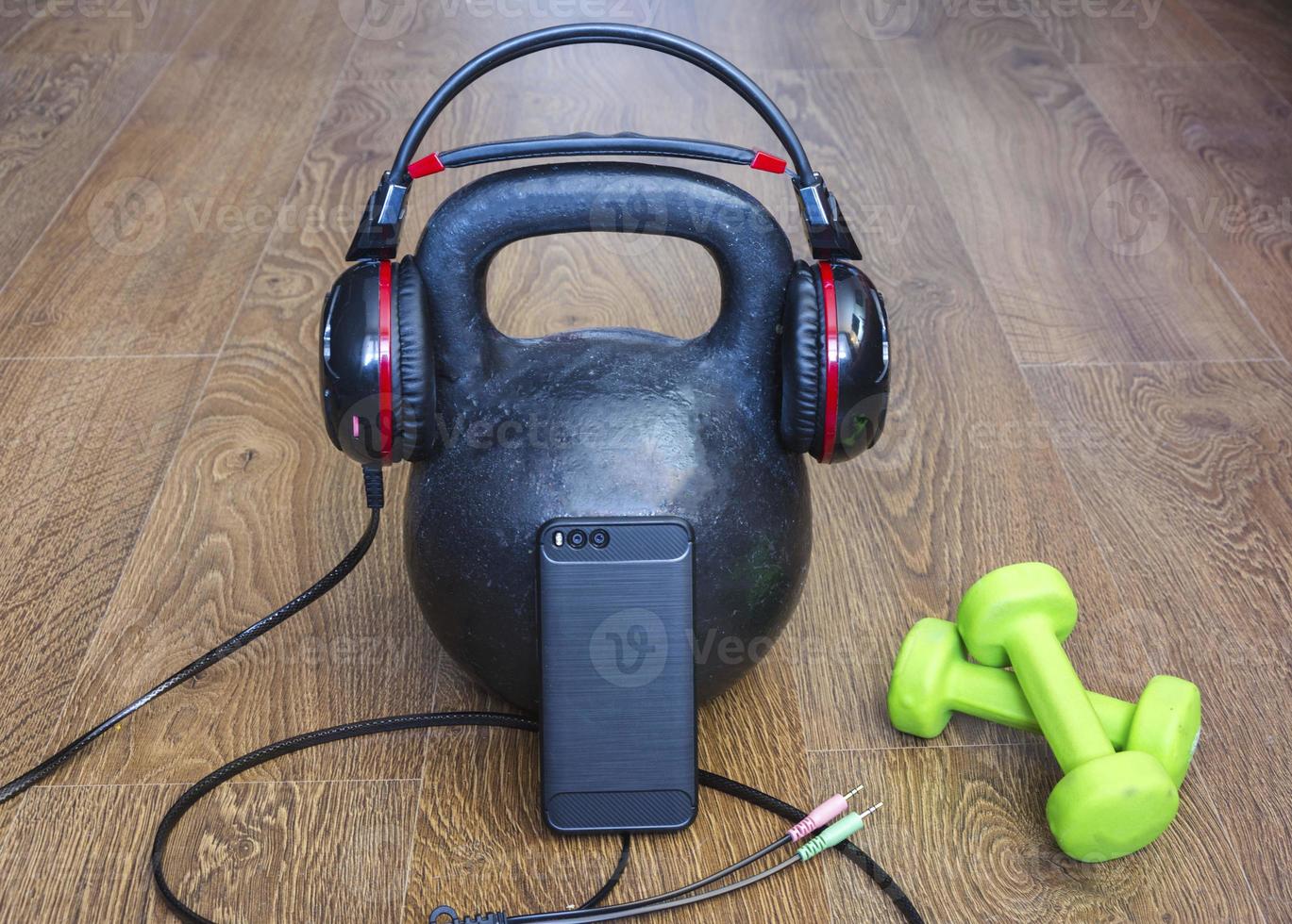 an old athletic kettlebell , athletics weight, dumbbells and smartphone with headphones on the floor. the concept of a healthy lifestyle and strength concept photo