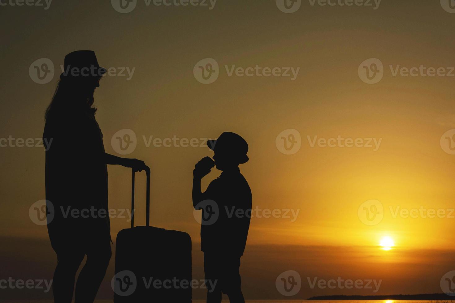 Mother and young son with a suitcase on the background of the sea sunset .A trip to the sea, a vacation, the ocean, a trip to warm countries photo