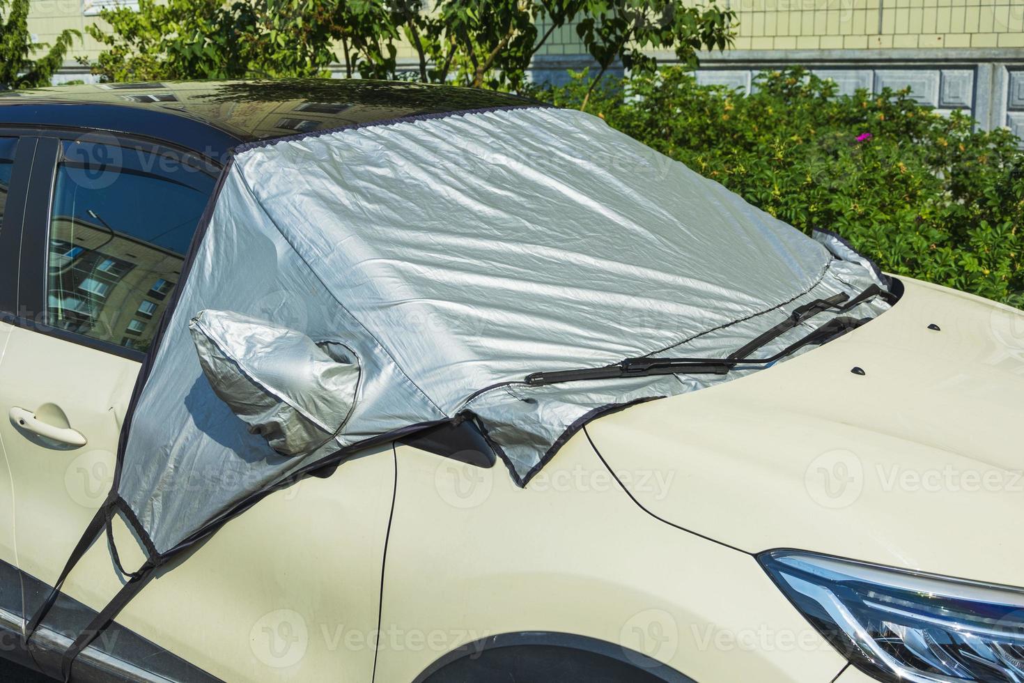 A car in a parking lot with a windscreen covered with a sunscreen reflector on the outside