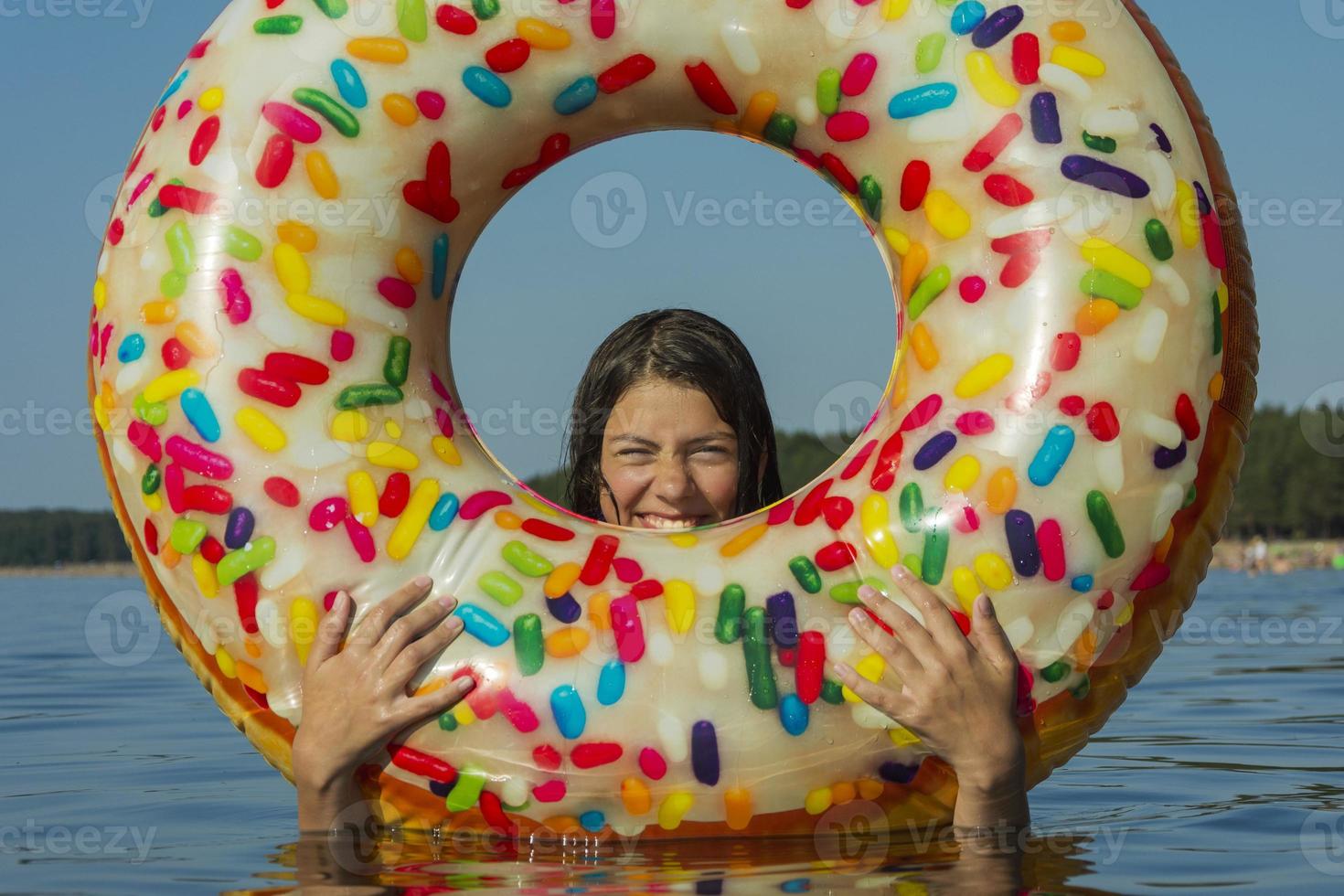 una linda adolescente con un colorido círculo de natación inflable nada en el agua azul del mar en un caluroso día soleado foto