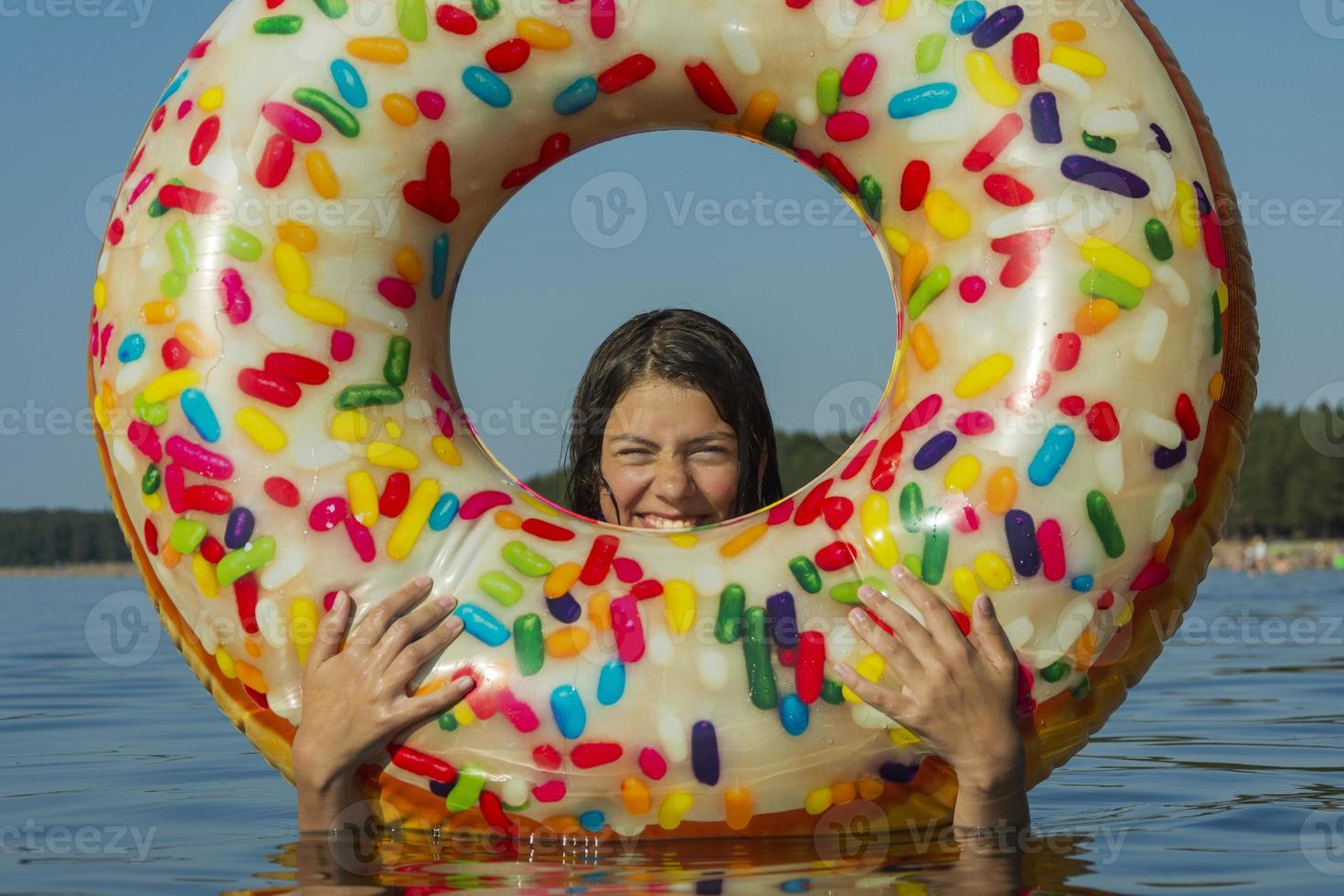 Cute teen girl with colorful inflatable swimming circle swims in the blue water of the sea on a hot sunny day photo