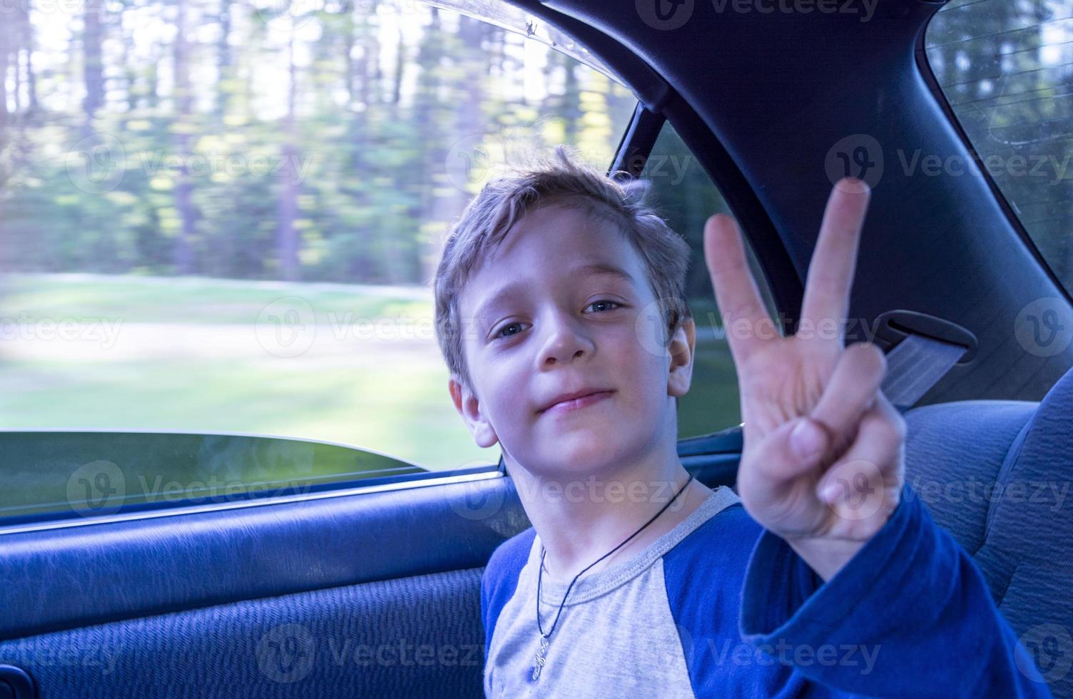 happy European boy rides in the car in the back seat, the child shows the victory sign, a view from inside the car photo
