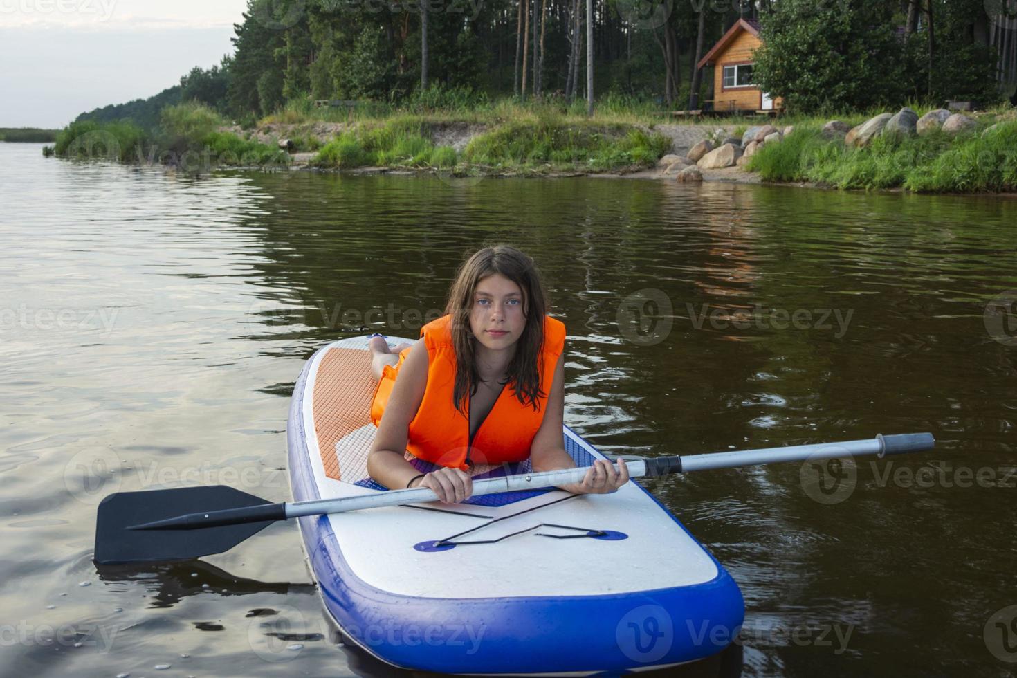 a teenage girl swims on a sup board, a beautiful girl rides a board with a paddle on a beautiful lake, river photo