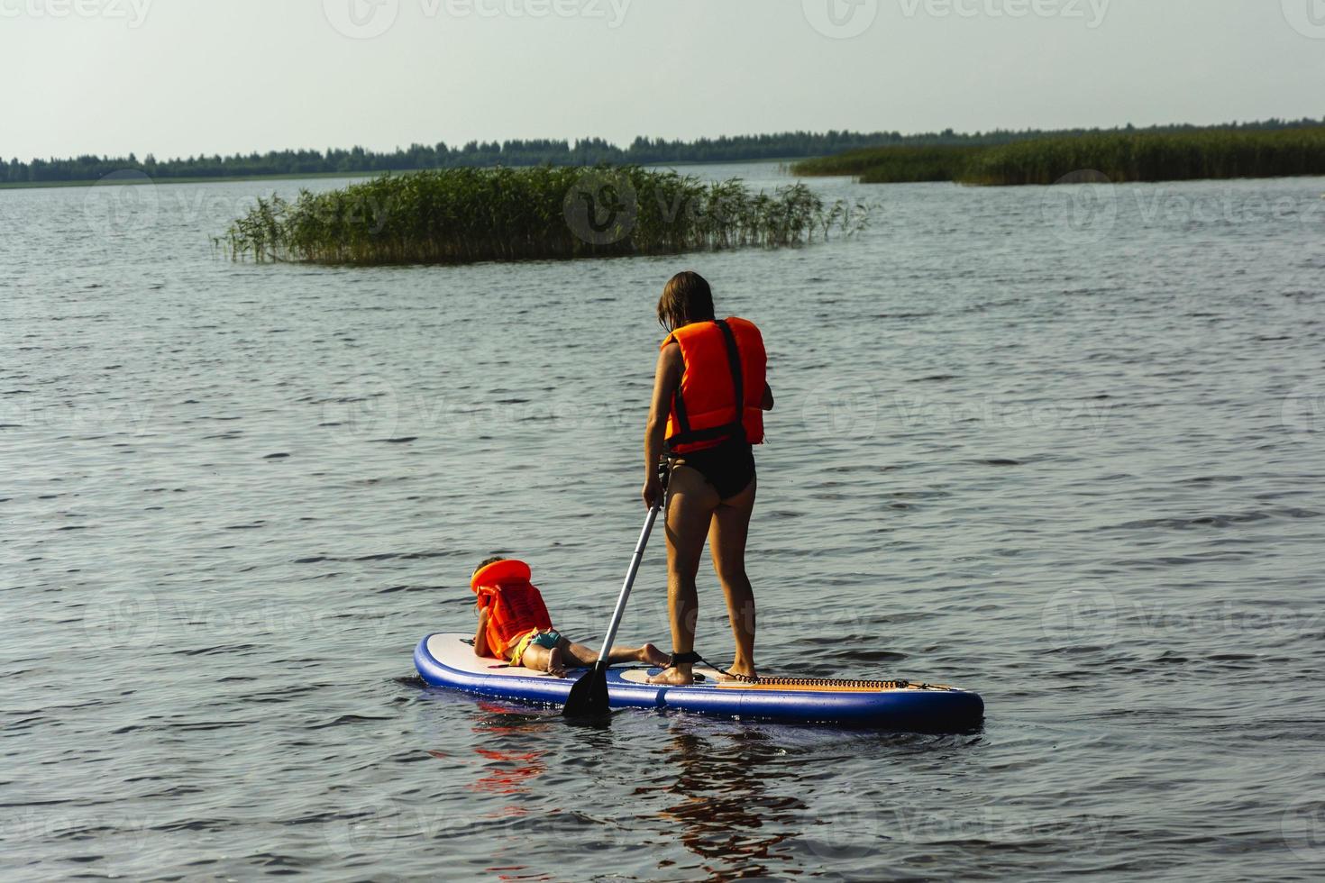 A young mother swims on a standing paddle board with her little daughter. SUP board. Water sports photo