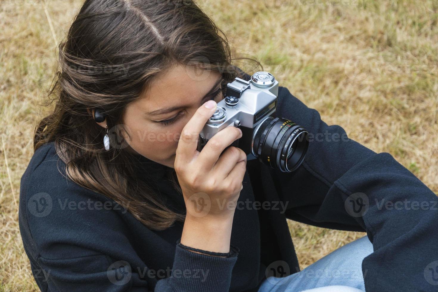 linda adolescente con una cámara, una chica tomando fotos en una cámara retro vintage en el césped del parque, un concepto de hobby