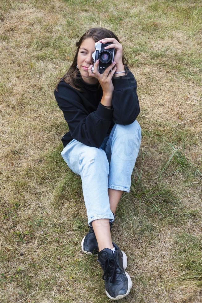 Cute teen girl with a camera, a girl taking pictures on a retro vintage camera on the grass in the park, a hobby concept photo