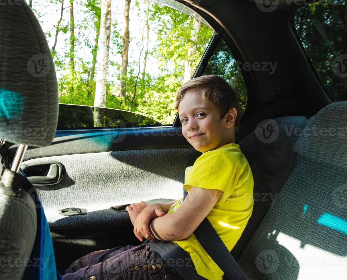 happy European boy rides in the car in the back seat, the child is smiling, he is wearing a seat belt photo