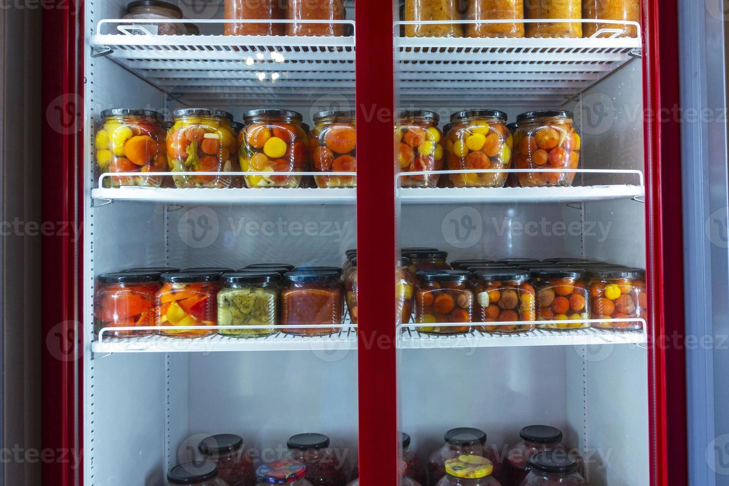 A refrigerated display case with cans of canned home products, a refrigerator with canned fruits and vegetables photo