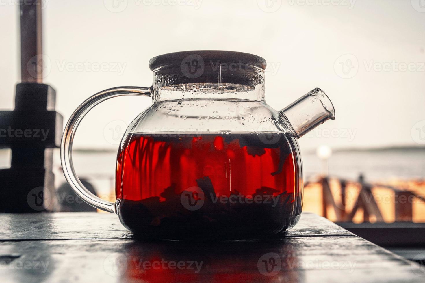 Tea in a glass teapot on a wooden table in the open air. Coastal cafe, brunch. The beach and the sea are blurred photo