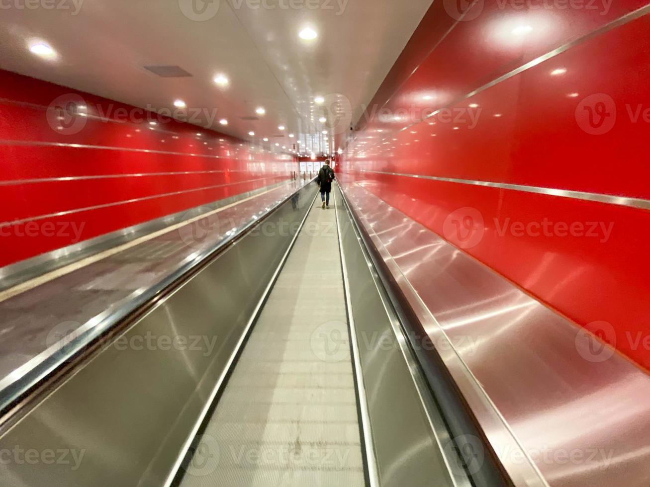 gran pasillo subterráneo rojo, moderno, largo y brillante entre estaciones de metro con andadores y escaleras mecánicas para el paso rápido de pasajeros foto
