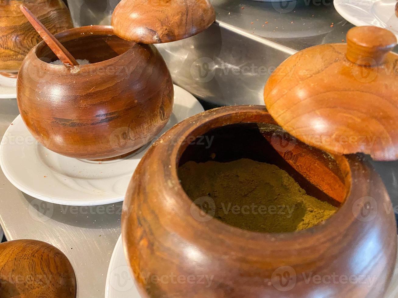 Small round wooden pots with spoons of spices and seasonings in a cafe or canteen photo