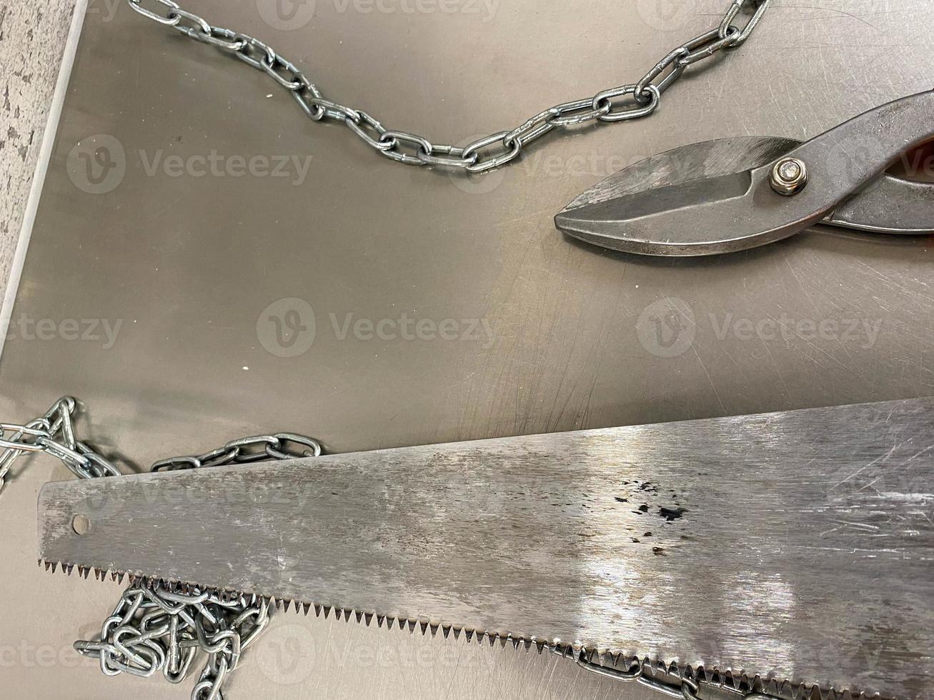 Large iron sharp metal scissors, metal cutters and a saw with chains lie on an iron table. Hand-held locksmith tools. The background photo