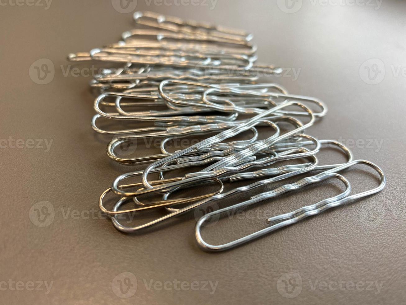 Shiny metal paper clips on a desktop with stationery in a business office. Close view photo