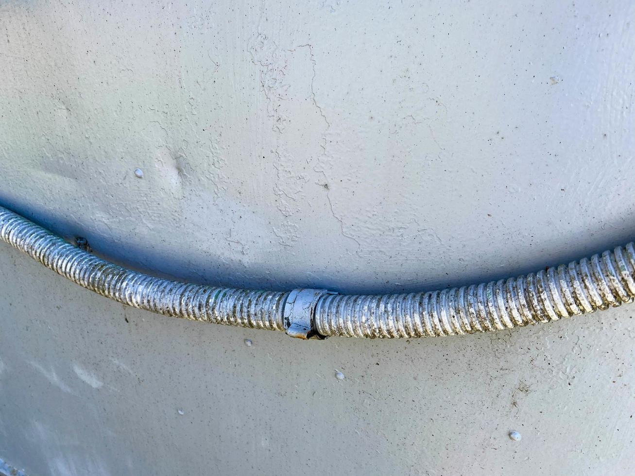 A large thick electric wire in a corrugated sheath on the background of a blue metal sheet of iron. Texture photo