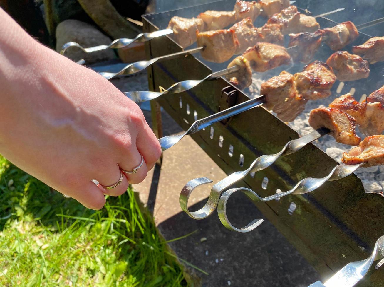 carne asada cocinada en brochetas en la mano del hombre. picnic al aire libre con parrilla barbacoa cocina foto