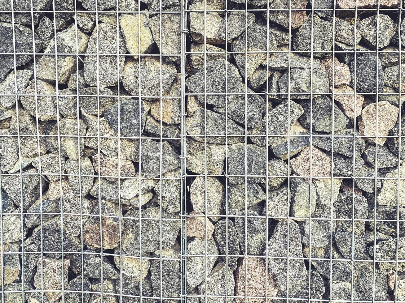 stones in a metal mesh. a mountain of gray, voluminous, structural stones lie in a metal structure as an element of decor. DIY fence for home photo