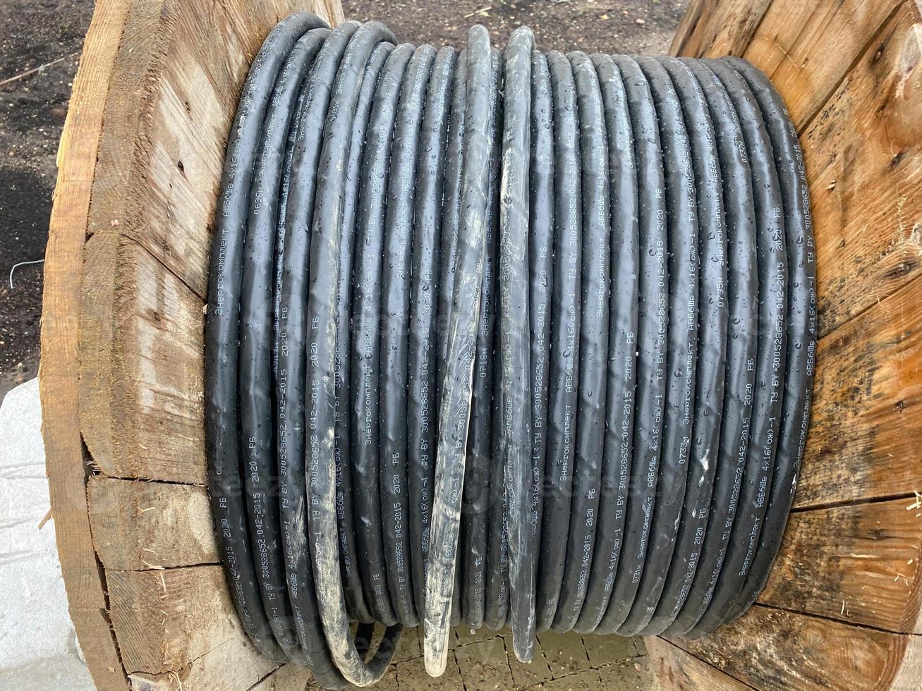 Large spool with black thick electrical wire or cable. Wooden coil with electrical industrial wires at a construction site photo