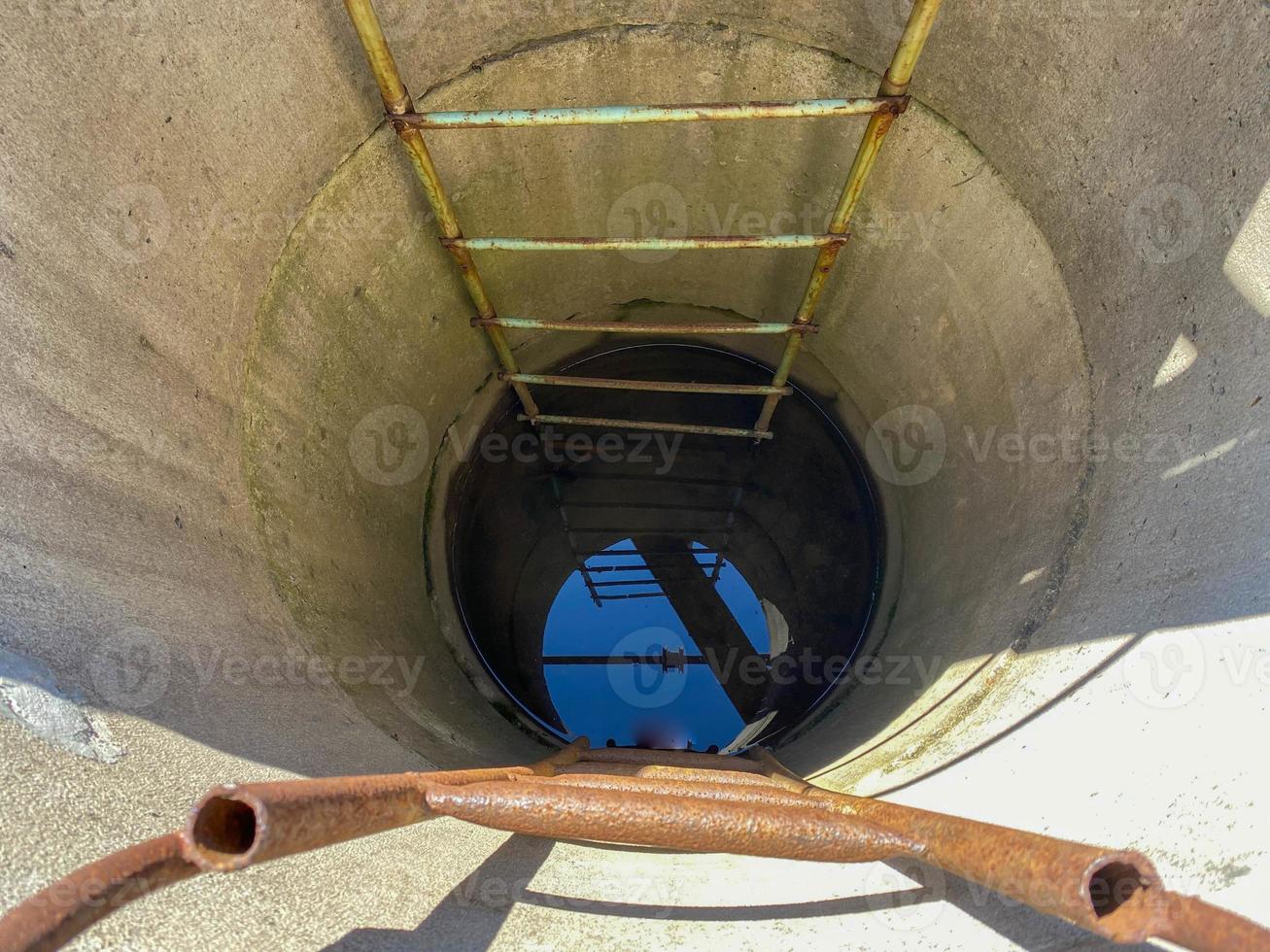 A large round deep well made of concrete rings with clean well underground water for drinking with old rusty stairs photo