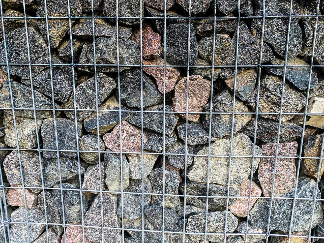 Texture of metal wire mesh and large stones cobblestones inside. The background photo