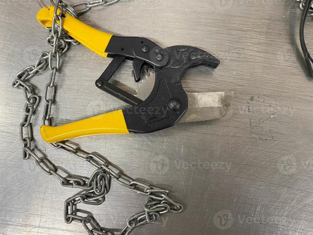 Large iron sharp metal scissors, metal cutters with chains, lie on an iron table. Hand-held locksmith tools. The background photo