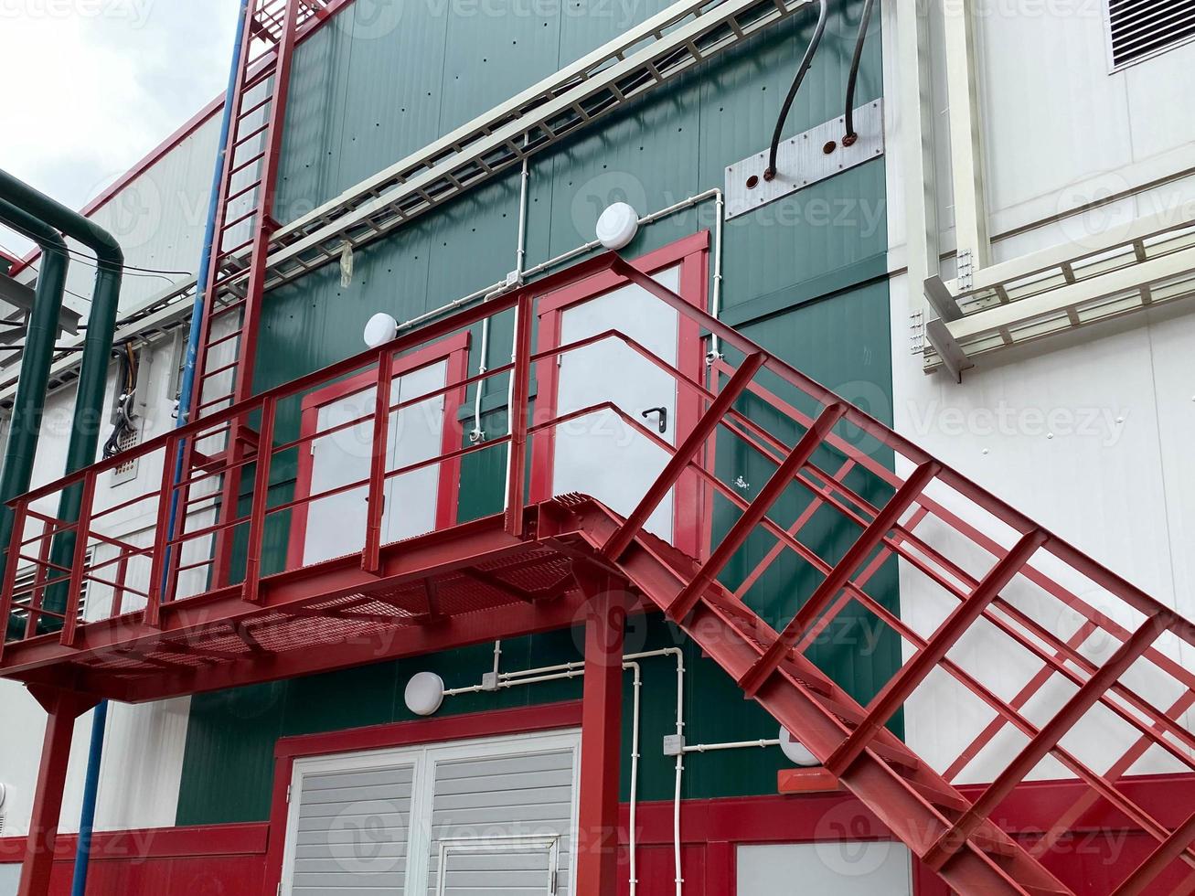 salida de emergencia con escaleras metálicas en la fachada de un edificio industrial, tienda, almacén, centro logístico. Escalera de hierro para hasta trabajos de mantenimiento. la escalera de acero está al lado de la pared del edificio foto